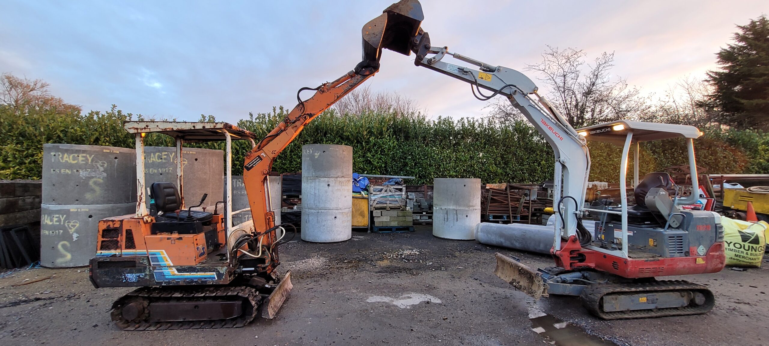 an old takeuchi digger with boom up against takeuchi tb219 excavator creating an arch with there buckets and booms