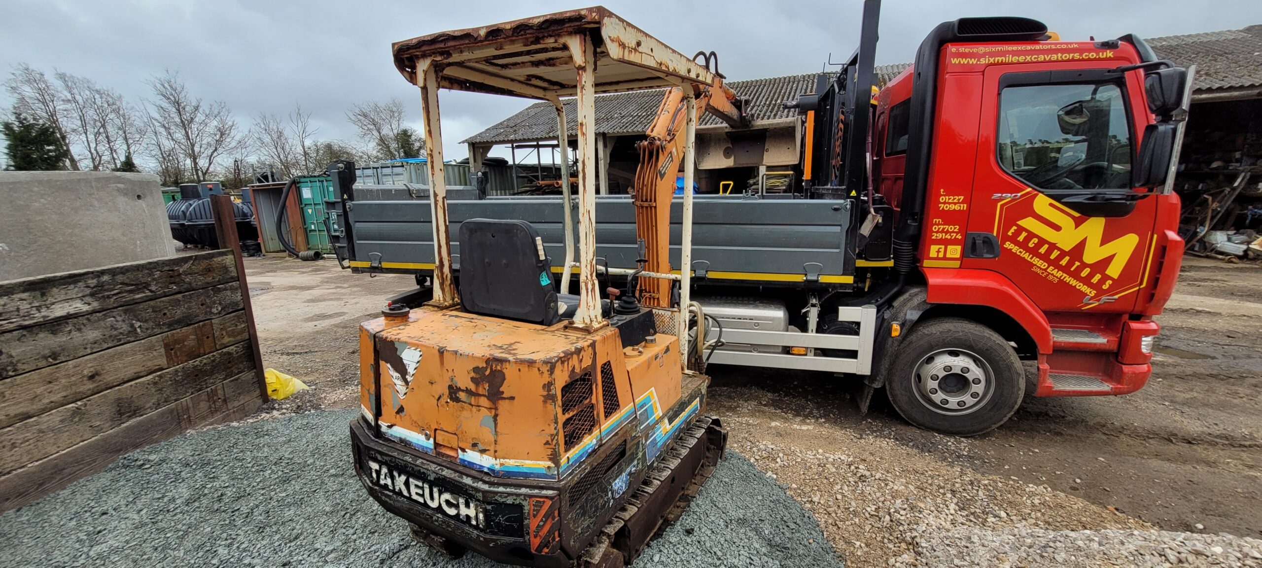 An old takeuchi digger painted in orange with boom over the side of a wagon