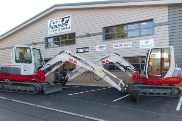 two takeuchi diggers parked up facing eachother. Each excavator has their boom crossing and parked in front of CBL Saltash Building