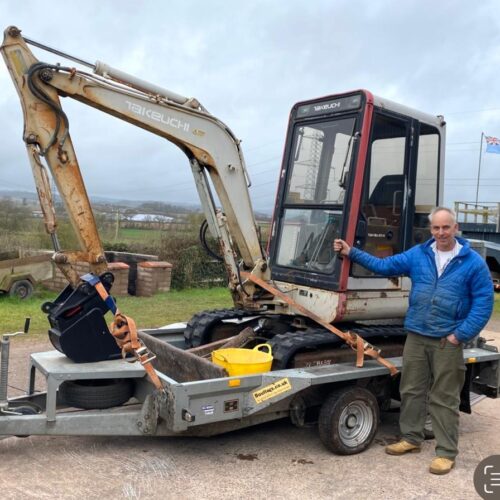 white takeuchi excavator on trailer with operator stood in front