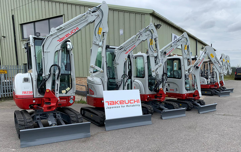 5 Takeuchi diggers in a row with a sign displaying the takeuchi. They are all in front of a green building that is Russells
