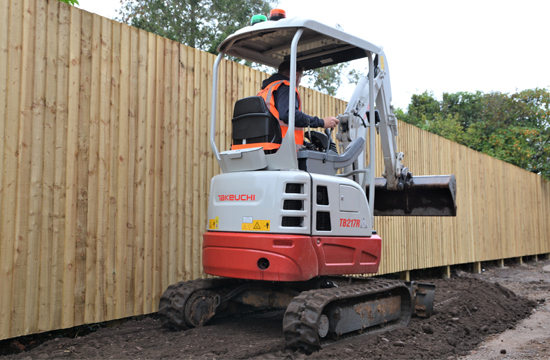 takeuchi tb217r from behind showing operating using the plant machinery. red and grey machine