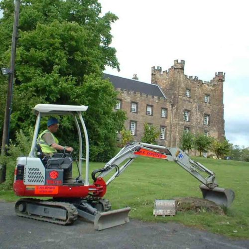 Takeuchi TB016 H.E Services digging in front of a castle
