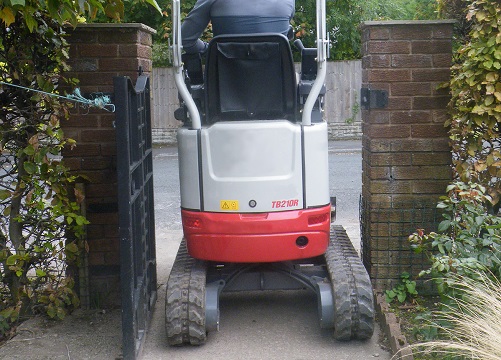 takeuchi tb210r micro digger 1 tonne fitting through a gateway in a front garden that a landscaper is operating